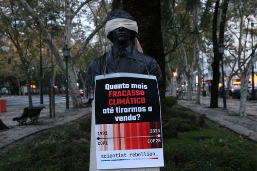 blindfolded bust with a sign that read quanto mais fracasso climático até tirarmos a venda