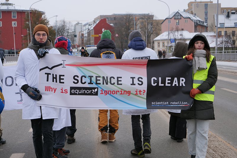 scientists holding a banner saying the science is clear why is equinor ignoring it while slow marching on a road