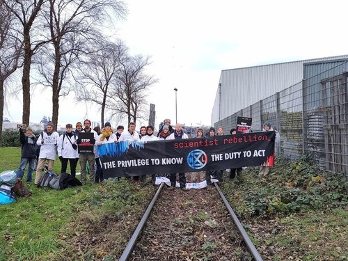 scientists hold a banner saying the privilege to know the duty to act while blocking a rail line